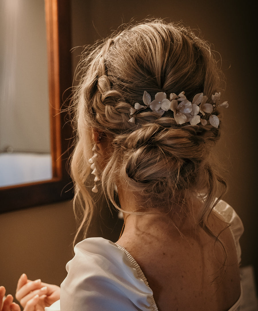Bride looking into mirror wearing flower bridal earrings and bridal headpiece also made in flowers.