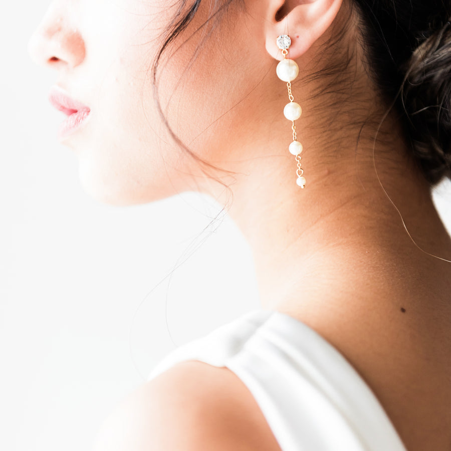 Bride with an elegant bridal bun is wearing a pair of long wedding pearl earrings. 
